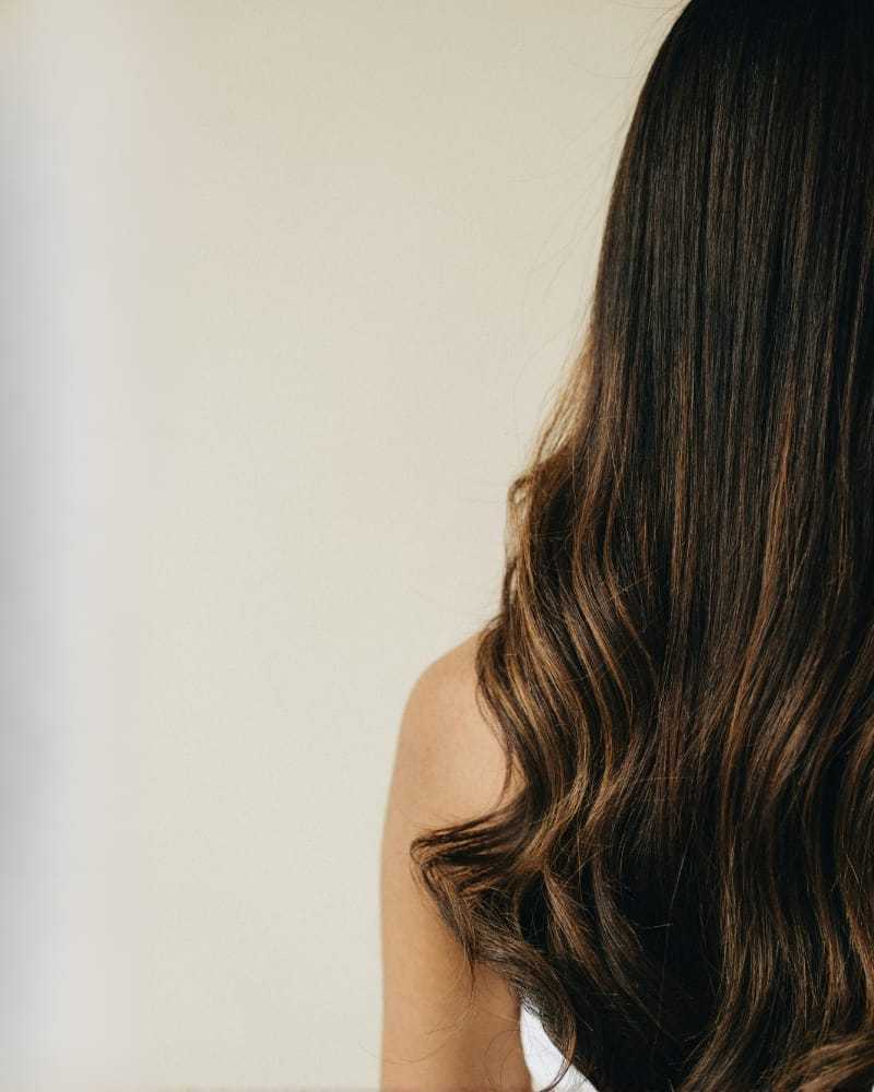 Long, wavy brunette hair cascading down a woman's back against a neutral background.