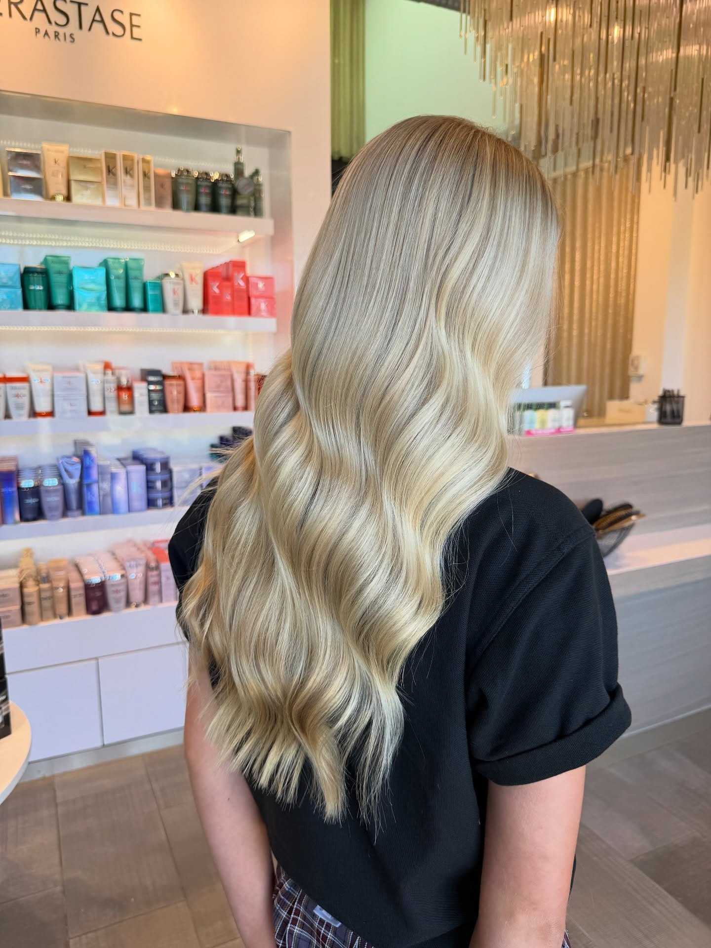 Blonde hair with soft waves at a salon, with a backdrop of haircare products on shelves.