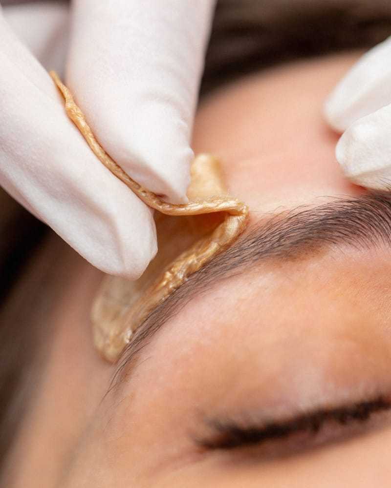 Eyebrow threading with hands in gloves, close-up view.