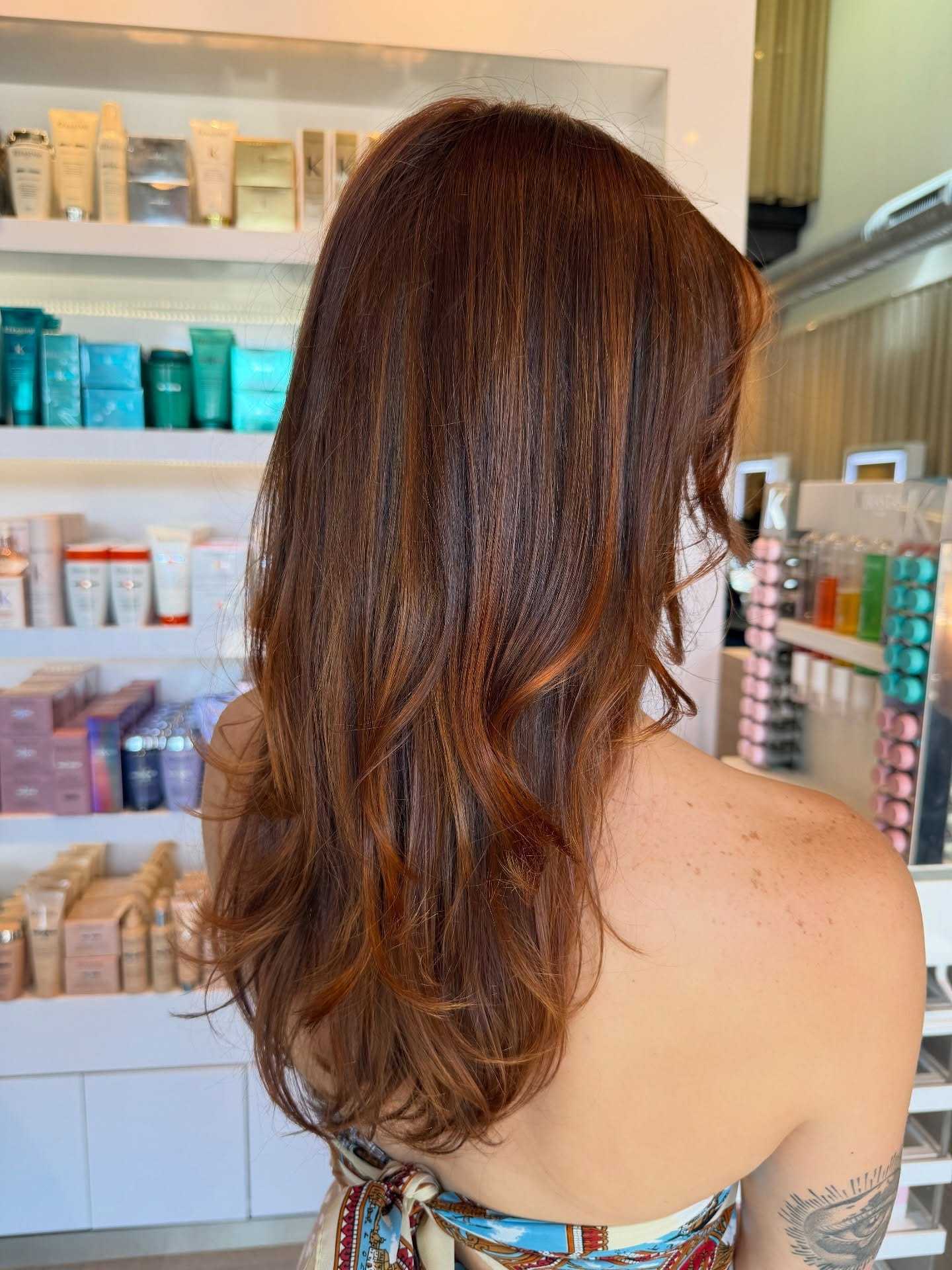 Long, wavy brown hair in a salon storefront with hair products on shelves.