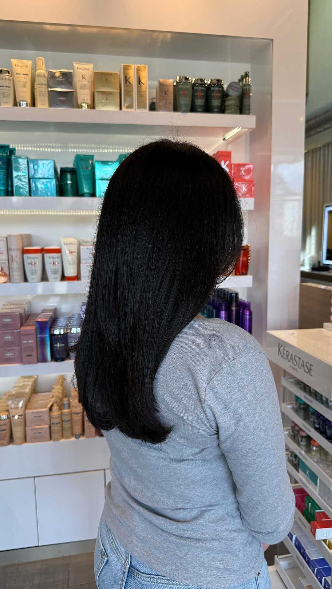 Woman with long dark hair in a salon, surrounded by hair products.