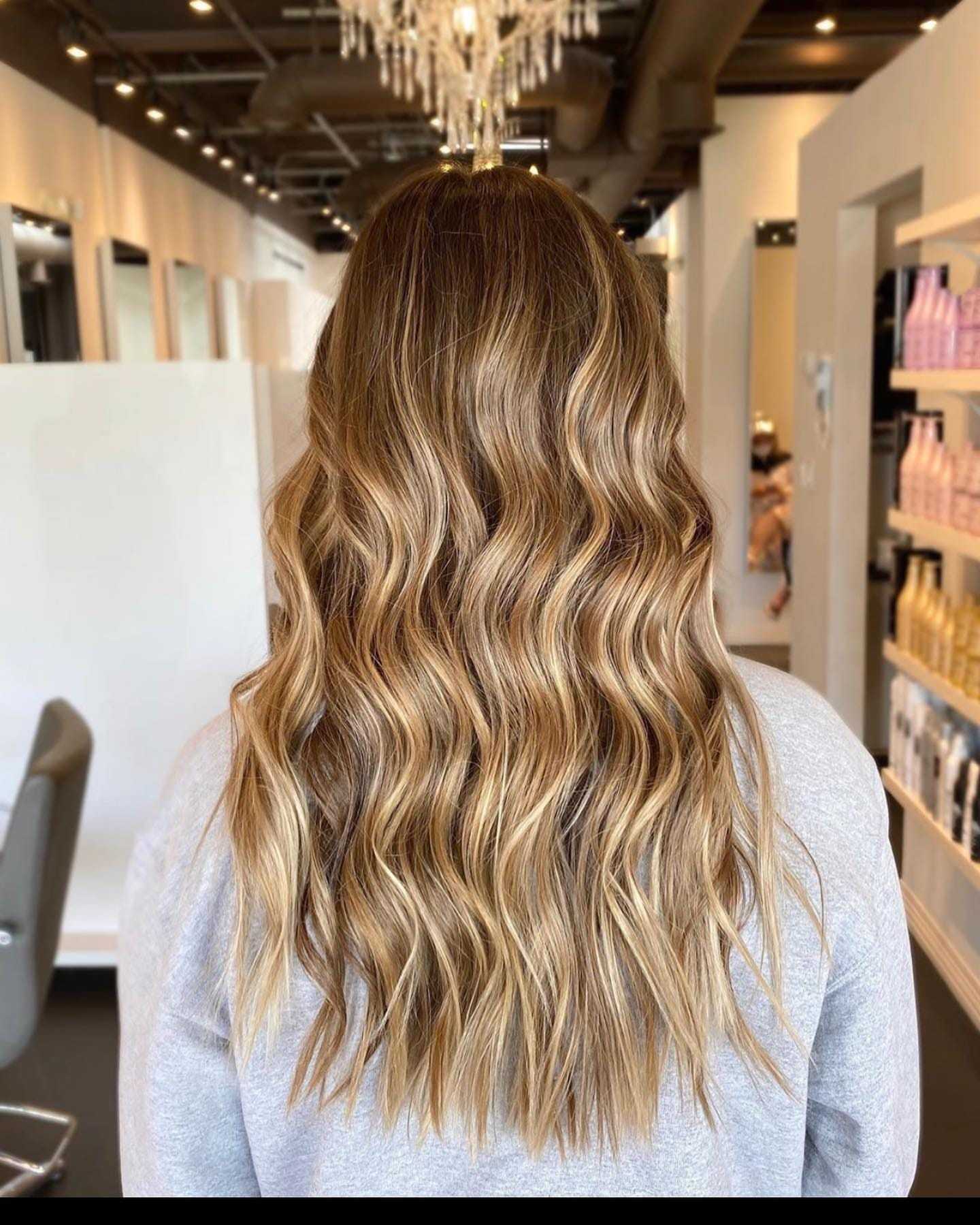 Wavy long brown hair with blonde highlights in a salon setting.